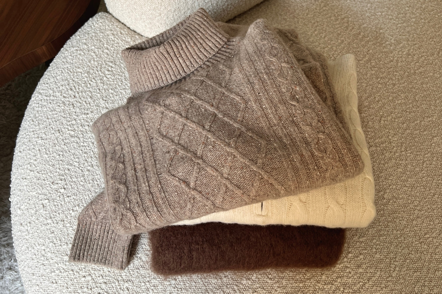 Vaalealla sohvalla on viikattu pino erilaisia neuleita.