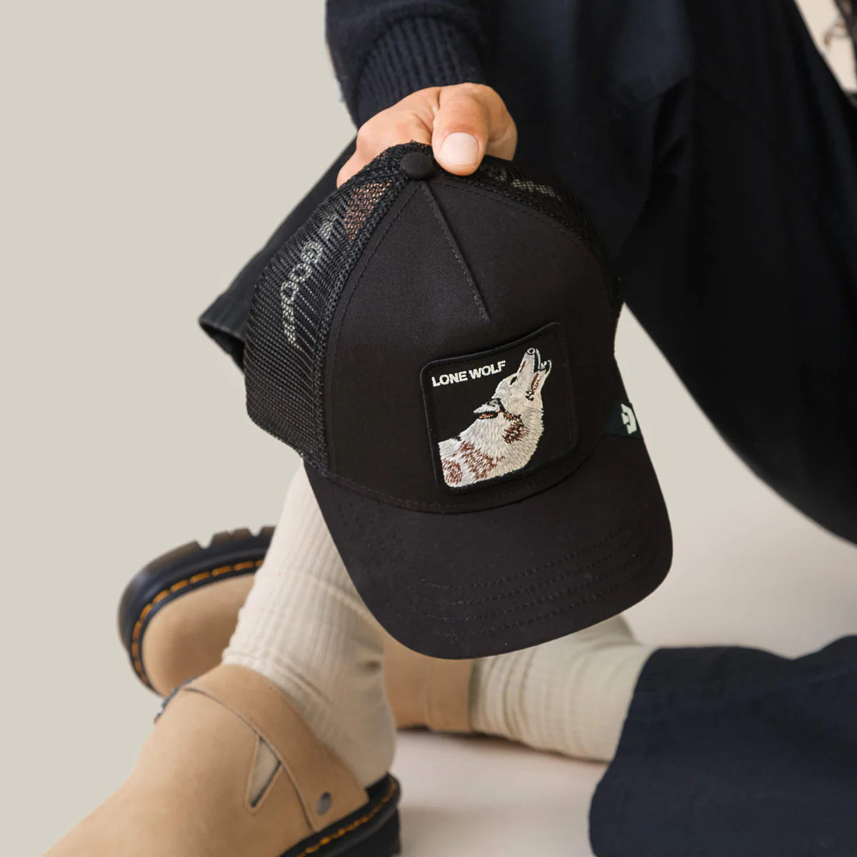 Goorin Bros lippis Lone Wolf Trucker, musta, jossa on musta verkkopäinen trucker-malli ja etuosassa valkoinen ja harmaa susiaiheinen merkki.