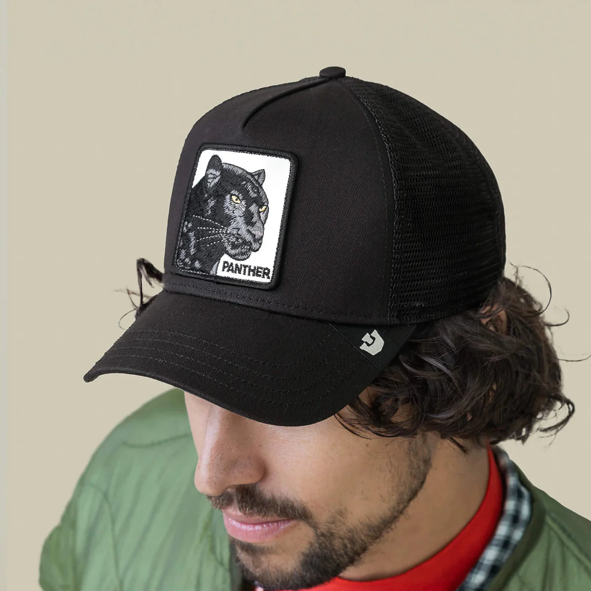 Goorin Bros lippis Panther Trucker All Black, musta, on musta verkkopäinen trucker-mallinen lippalakki, jossa etuosassa panterin kuvalla varustettu merkki ja kaareva lippa.