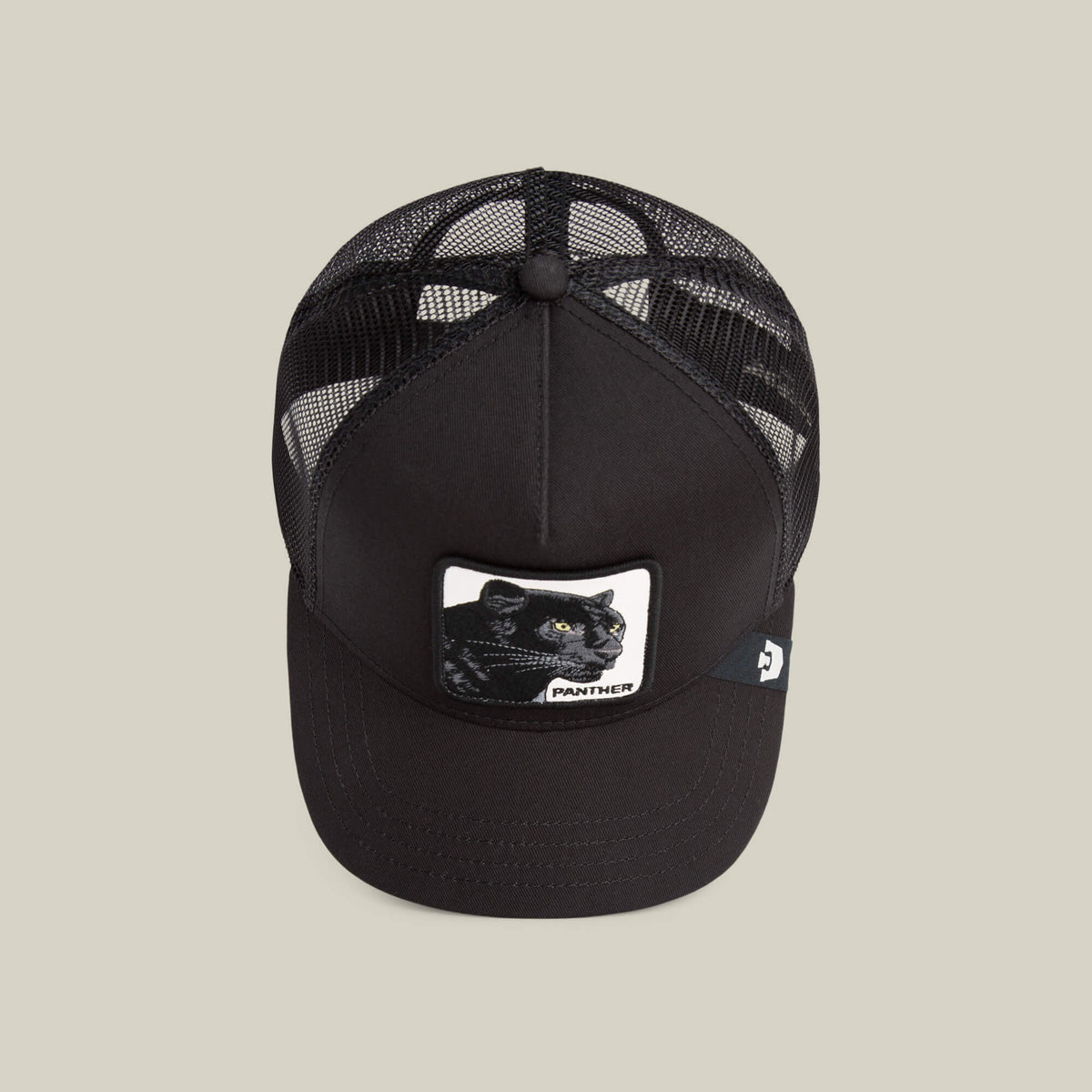 Goorin Bros lippis Panther Trucker All Black, musta, jossa musta verkkopäällinen, jämäkkä etuosan kangas ja panterikuvioinen brodeerattu merkki etupaneelissa.