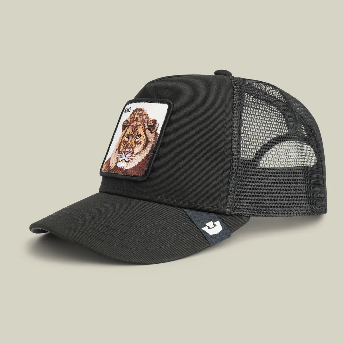 Goorin Bros lippis Lion King Trucker, musta, jossa musta etumateriaali ja verkkopäällinen, etuosassa kirjailtu leijonan kuva, suorakaiteen muotoinen merkki ja lievä kaareva lippa.