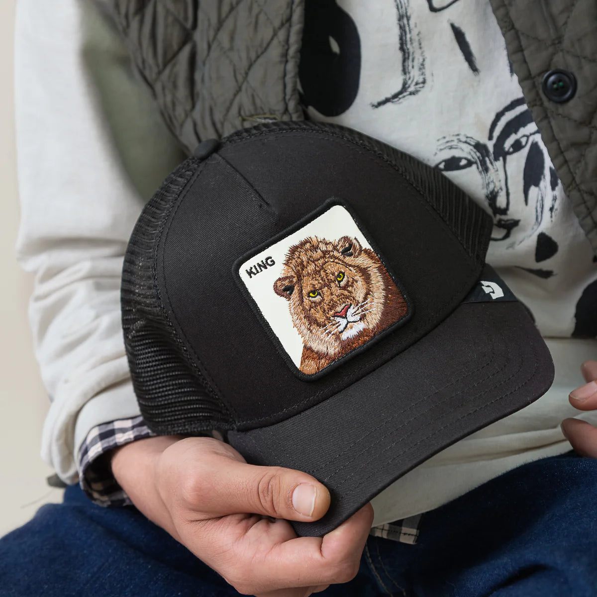 Goorin Bros lippis Lion King Trucker, musta, verkkomainen takaosa, musta etupaneeli ja lippa sekä lion-kuviointi valkoisella taustalla edessä.