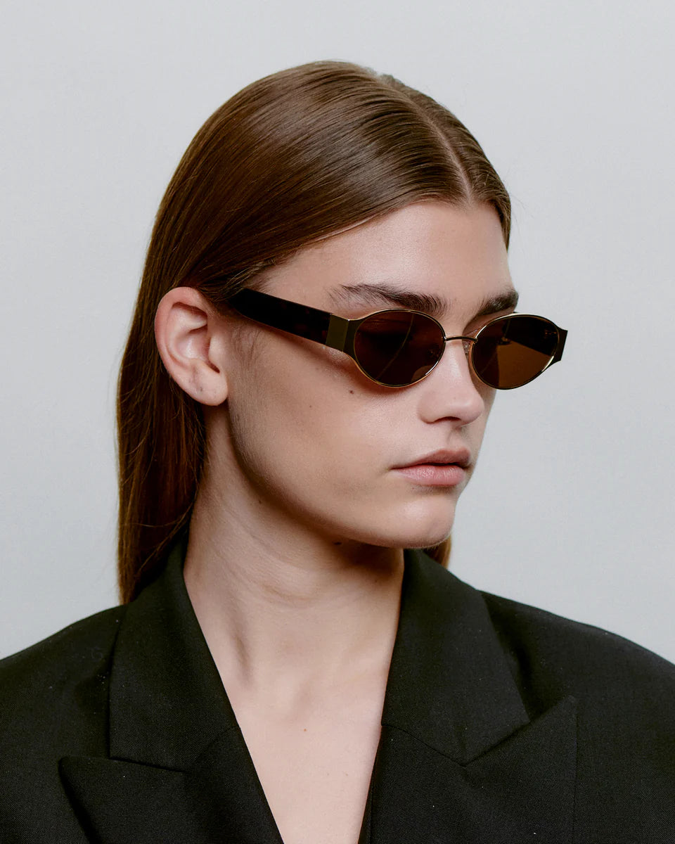 A.Kjaerbede unisex aurinkolasit Bella, Kulta, joissa on ohuet, kullanväriset metallikehykset ja tummat soikeat linssit, moderni ja minimalistinen muotoilu.
