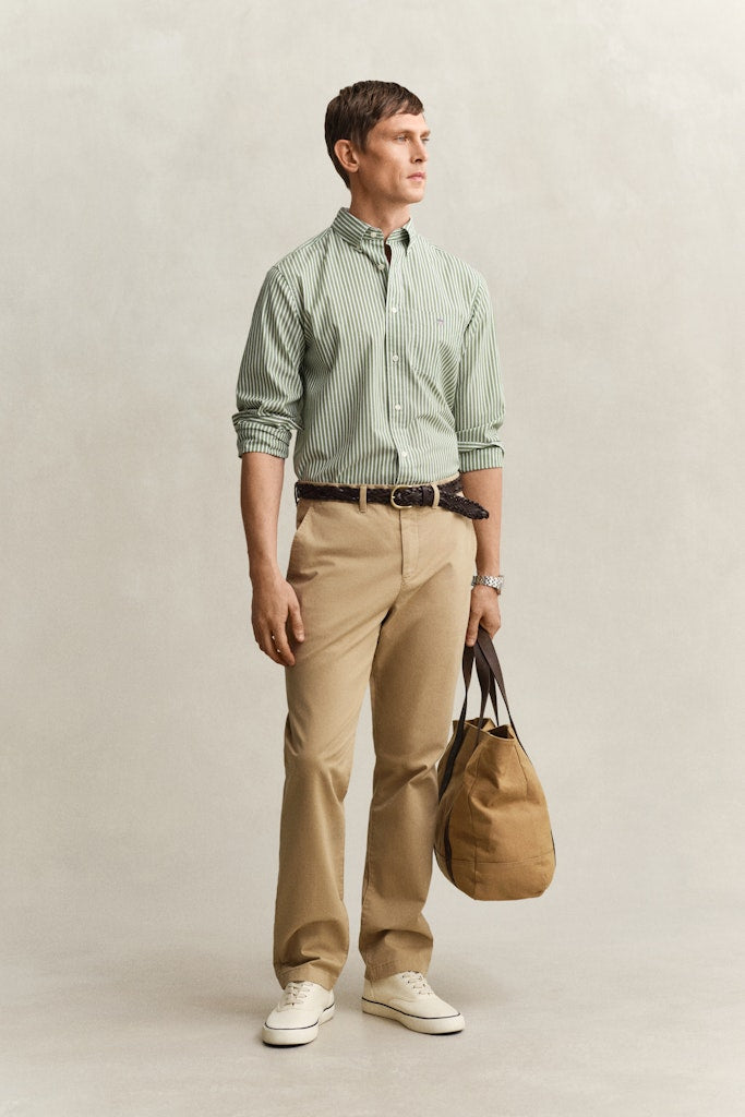 Mies pukeutunut vaalean beigen sävyisiin Gant miesten chinot Classic Chinos, Beige -housuihin, joissa on suora leikkaus ja kevyt, kestävä materiaali.