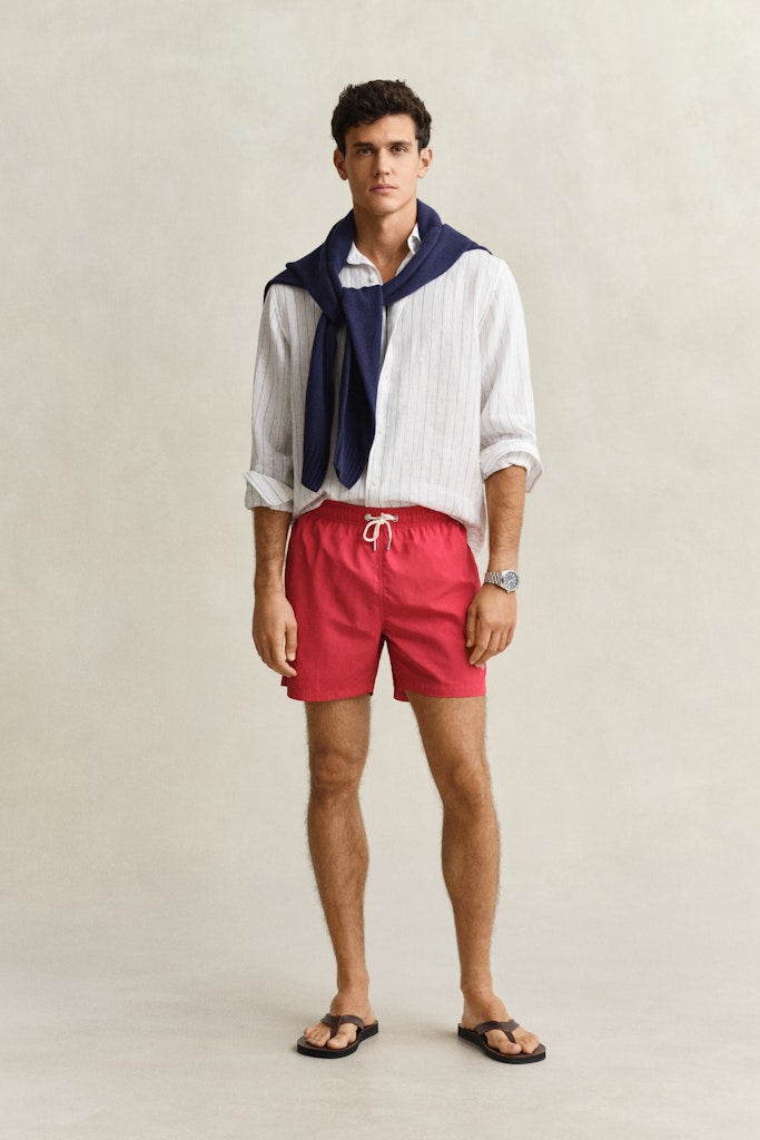 Mies käyttää Gant miesten uimashortsit Classic Fit Swim Shorts, punainen -shortseja, joissa on suora leikkaus, kirkas punainen väri ja säädettävä vyötärönauha.