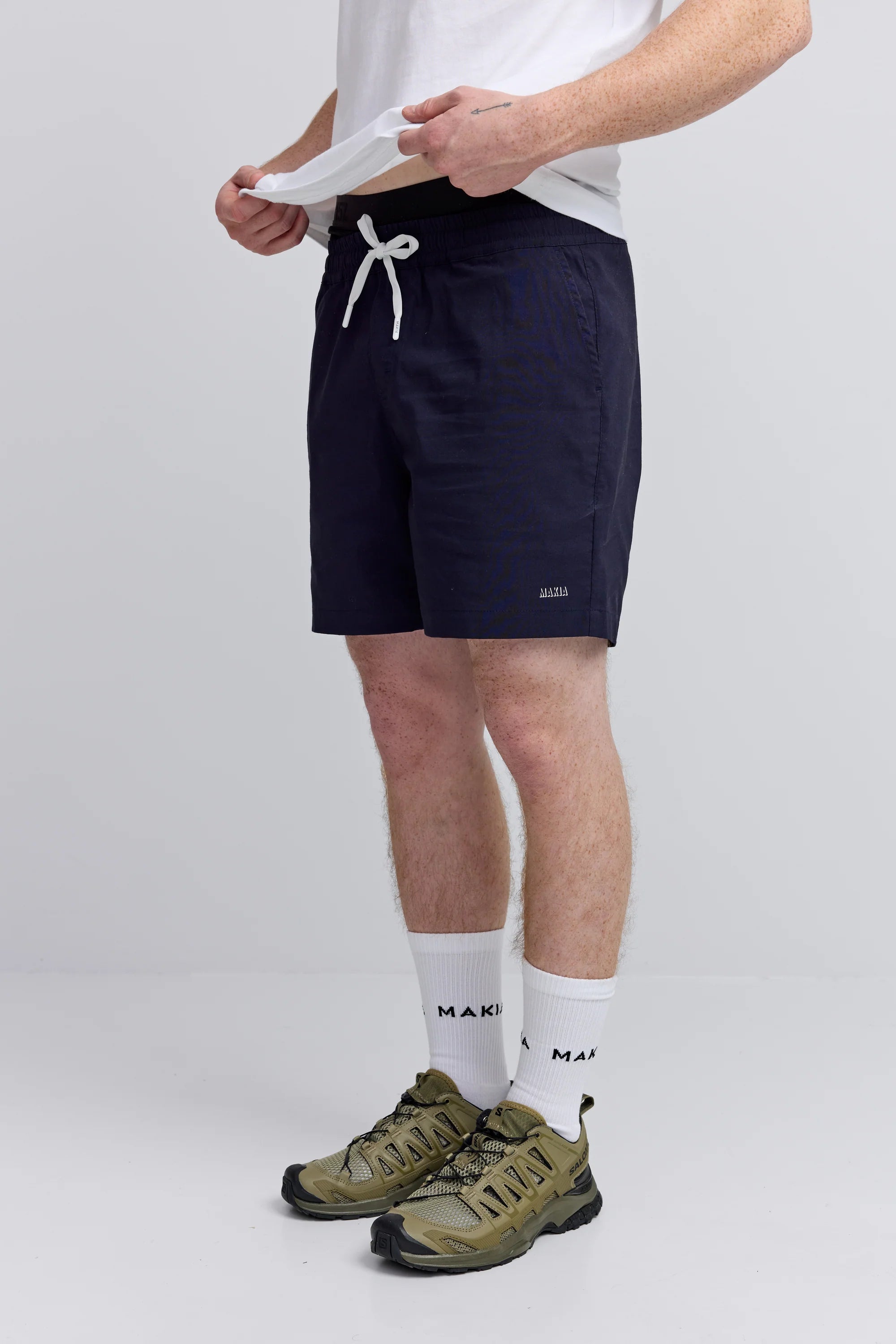 Makia miesten shortsit Shadow Hybrid Shorts, tummansininen, suoraleikkauksella ja kuminauhavyötäröllä, jossa on valkoinen nyöritys ja pienellä logolla koristeltu etureuna.