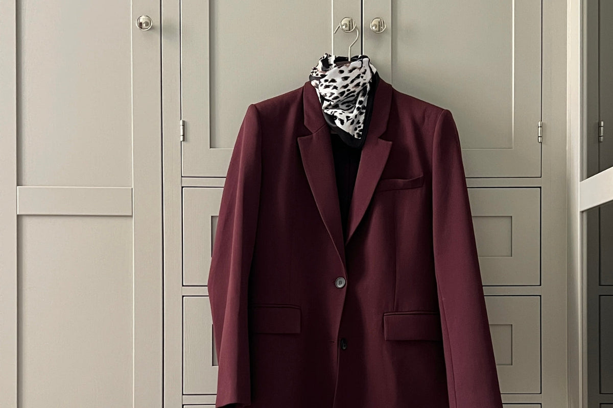 Vaatekaapin oven nupissa roikkuu henkarilla viininpunainen bleiseri. Kaapin edessä on lattialla viininpunainen laukku sekä nilkkurit.