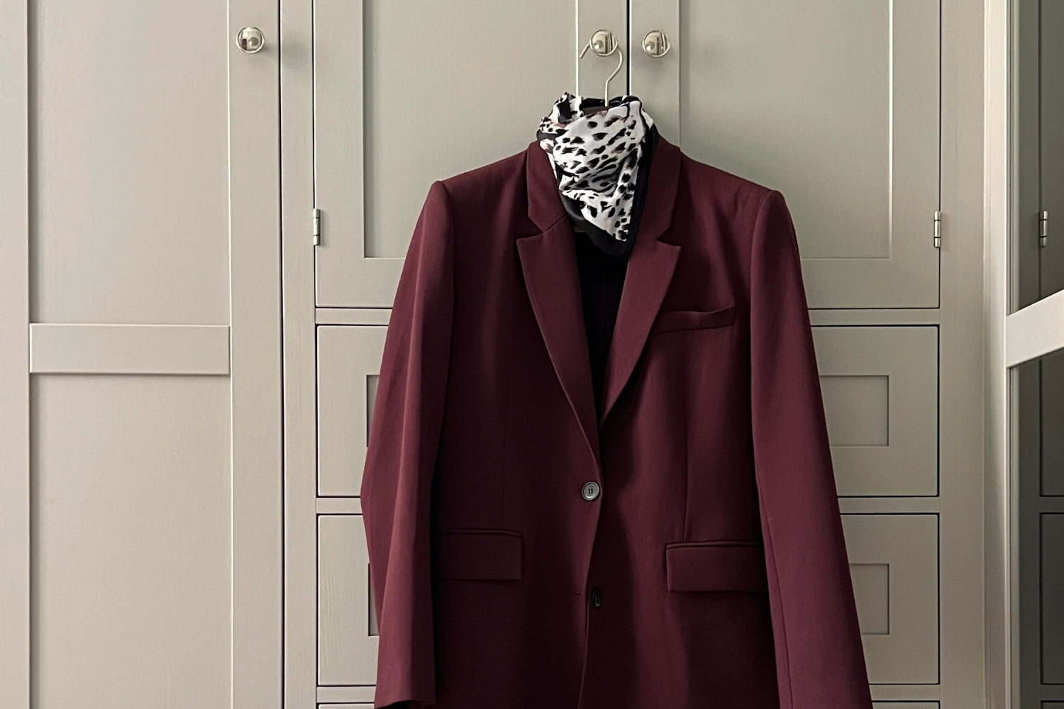 Vaatekaapin oven nupissa roikkuu henkarilla viininpunainen bleiseri. Kaapin edessä on lattialla viininpunainen laukku sekä nilkkurit.