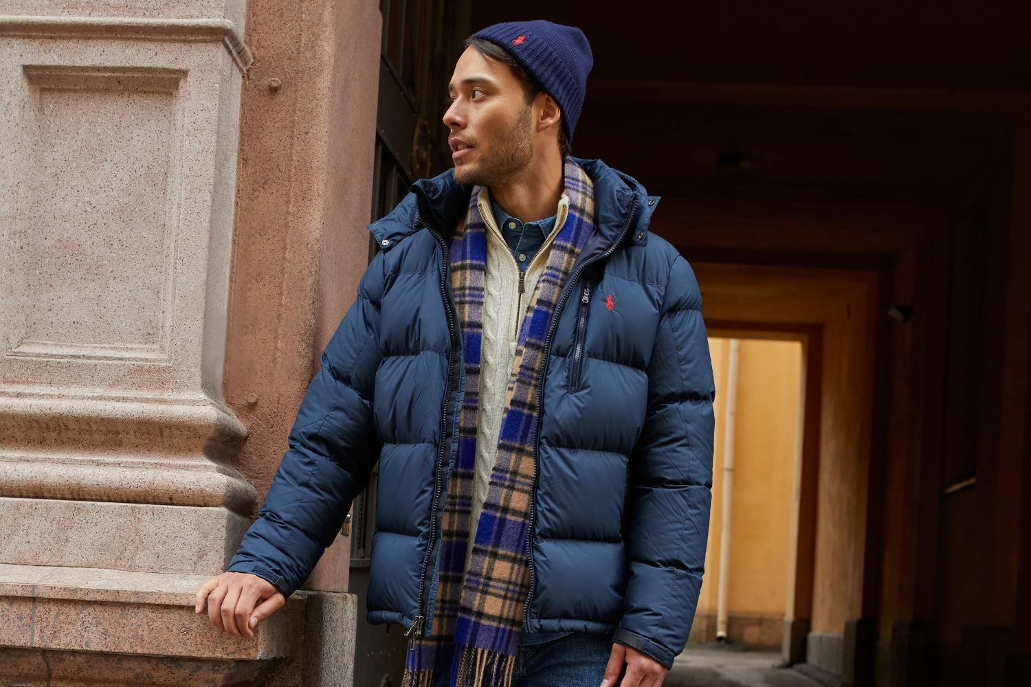 Mies seisoo talon sisäänkäynnillä. Hän on pukeutunut muhkeaan, tummansiniseen untuvatakkiin.