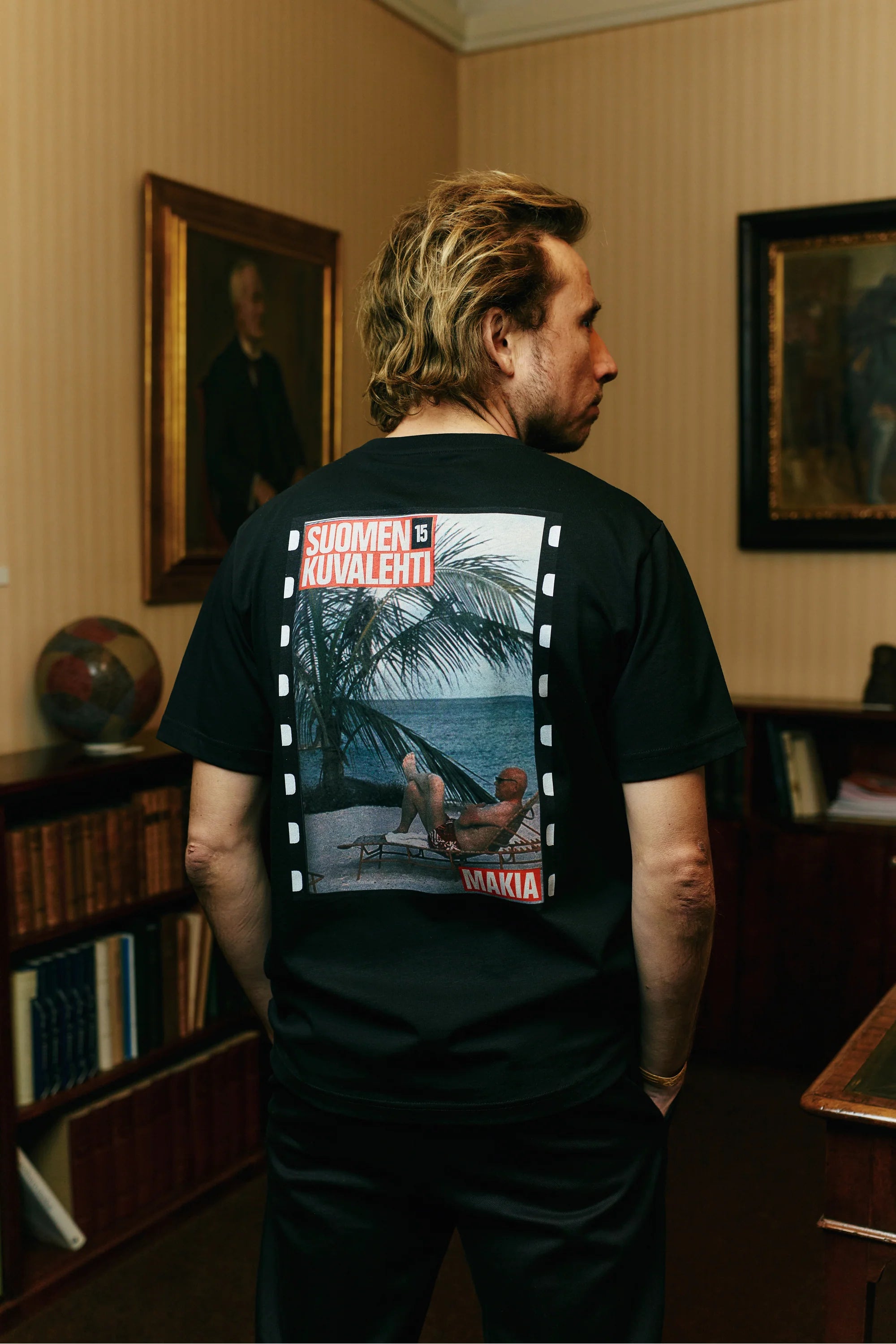 Makia miesten t-paita Kekkonen T-Shirt, musta, jossa on suoraleikkaus, lyhyet hihat ja takana suuri valokuvatyylinen printti merimaisemalla ja teksteillä.